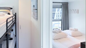 A hotel room with a bunk bed on the left and a single bed on the right. There is a window with a view of buildings outside.
