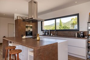 A modern kitchen with a central island, built-in oven, and a large window offering a view of the outdoors. - Villa LAETIZIA- 5 bedrooms, swimming pool, sea view (PIETROSELLA)