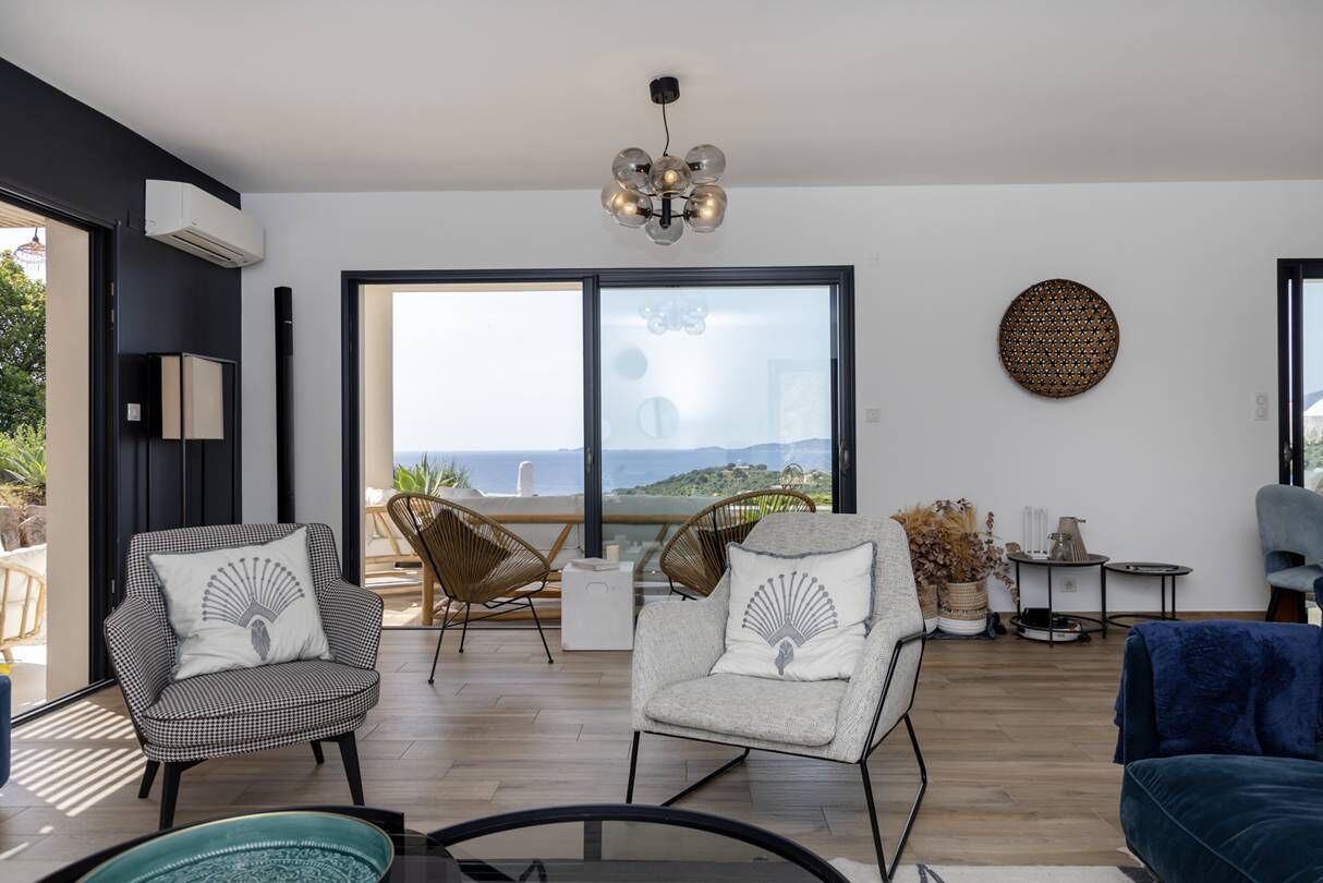 Un salon moderne avec deux fauteuils, un canapé, un lustre et une grande fenêtre donnant sur un beau paysage.