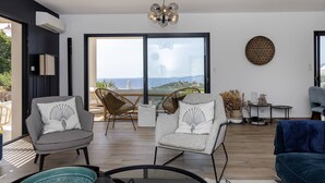 A modern living room with two armchairs, a sofa, a chandelier, and a large window with a view. - Villa LAETIZIA- 5 bedrooms, swimming pool, sea view (PIETROSELLA)