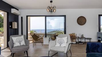 Un salon moderne avec deux fauteuils, un canapé, un lustre et une grande fenêtre donnant sur un beau paysage.