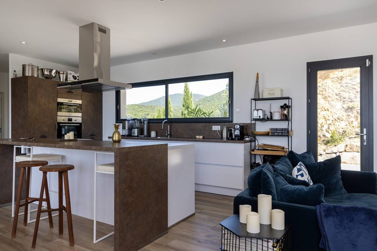 Une cuisine moderne dotée d’un îlot central, de tabourets de bar et offrant une vue sur l’extérieur.