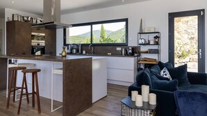 A modern kitchen with a central island, bar stools, and a view of the outdoors. - Villa LAETIZIA- 5 bedrooms, swimming pool, sea view (PIETROSELLA)