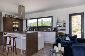 A modern kitchen with a central island, bar stools, and a view of the outdoors. - Villa LAETIZIA- 5 bedrooms, swimming pool, sea view (PIETROSELLA)