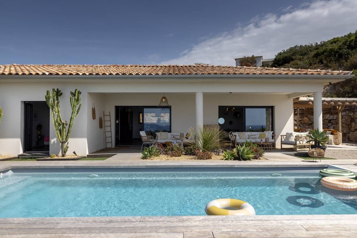 A modern house with a swimming pool, outdoor seating, and a view of the sea.