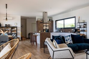 A modern kitchen with a central island, a dining area with wicker furniture, and a living room with a dark blue sofa. - Villa LAETIZIA- 5 bedrooms, swimming pool, sea view (PIETROSELLA)