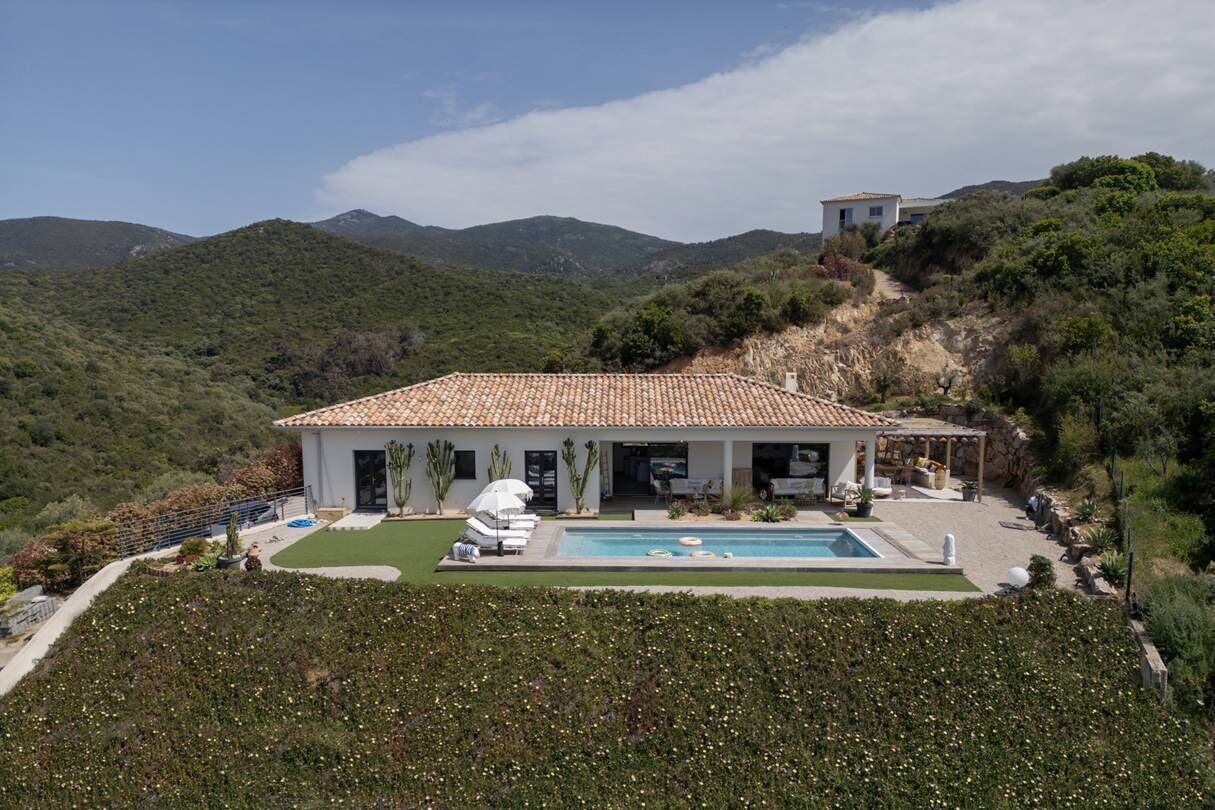 Une villa avec piscine, entourée d’une végétation luxuriante et de collines.