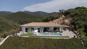 Une villa avec piscine, entourée d’une végétation luxuriante et de collines.