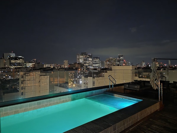 Piscina no terraço com vista para a cidade à noite.