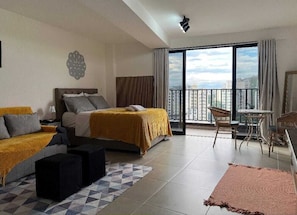 Quarto de hotel com cama, sofá, mesinha, cadeira e varanda com vista.