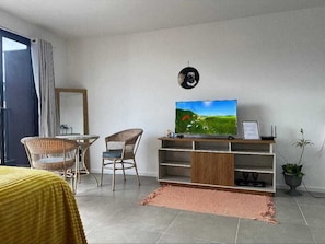 A modern living room with a flat-screen TV, wicker chairs, a small table, a sofa, and a potted plant. - Charming and comfortable studio in Lapa | Perfect location | Pool and tranquility (Rio de Janeiro)
