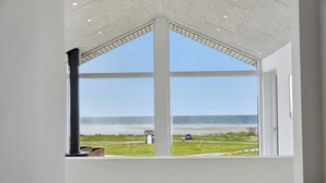 Une pièce dotée d’une grande fenêtre donnant sur la mer et une zone verdoyante.