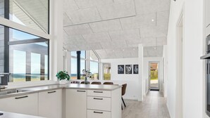 Une cuisine moderne dotée d’un grand îlot central, de meubles blancs et offrant une vue sur l’océan.
