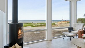 Un intérieur moderne avec un poêle à bois, de grandes fenêtres et une vue sur la plage.