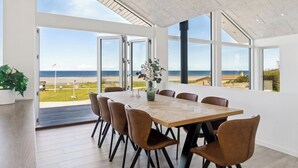 Un vaste espace dédié à la salle à manger, avec une grande table et des chaises, de grandes fenêtres offrant une vue sur la plage et un design moderne au niveau du plafond.
