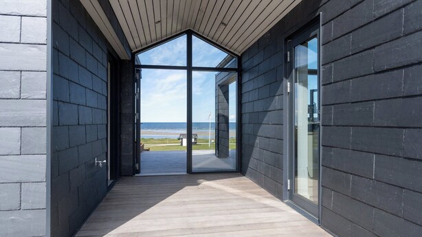 Un bâtiment moderne doté d’une terrasse en bois et de grandes portes vitrées donnant sur une vue imprenable sur la plage.
