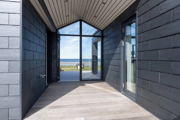 Ein modernes Gebäude mit einer Holzterrasse und großen Glasfenstern, die Blick auf den Strand bieten.