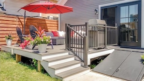 Une terrasse avec un parasol rouge, des meubles d’extérieur et des plantes en pot.