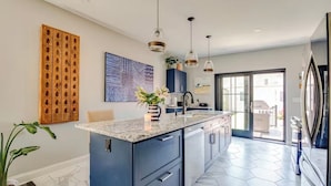 Une cuisine moderne dotée d’un îlot central, de luminaires suspendus et offrant une vue sur l’extérieur.