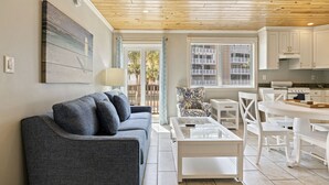 A modern living room with a grey sofa, a glass coffee table, and a white dining table with chairs. - Sunset and Sunrise - With Pool next to Beach! (St. Pete Beach)