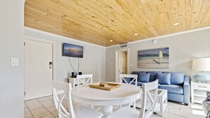 A room with a wooden ceiling, a round white table with chairs, a blue sofa, and a TV mounted on the wall. - Sunset and Sunrise - With Pool next to Beach! (St. Pete Beach)