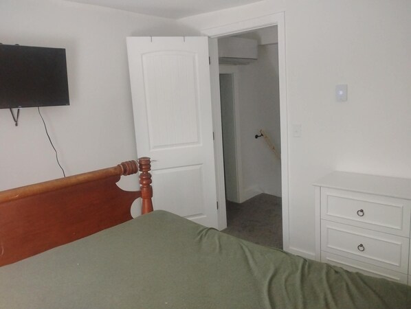 Un dormitorio con una cama, cabecera de madera, cómoda blanca y televisor montado en la pared.