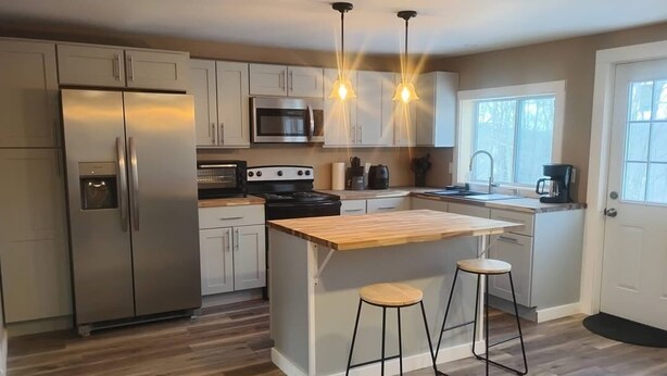 A modern kitchen with stainless steel appliances, a wooden island, bar stools, and pendant lighting.