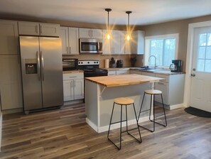 Una cocina moderna con electrodomésticos de acero inoxidable, una isla de madera, taburetes de bar e iluminación colgante.