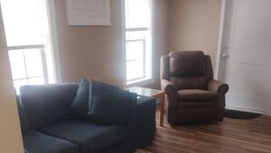A living room with a dark blue sofa, a brown armchair, and a patterned rug on wooden flooring.