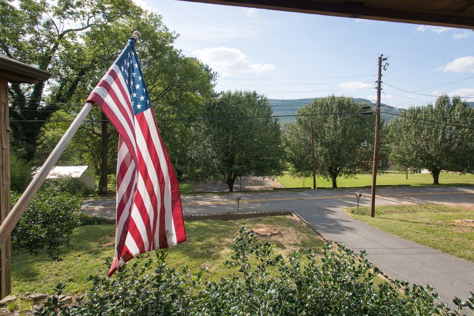 Eine amerikanische Flagge an einem Fahnenmast in einer Wohngegend mit einer asphaltierten Straße, Bäumen und einer Rasenfläche.