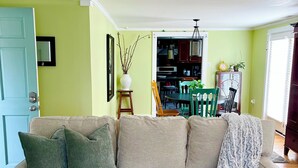 Un salon avec un canapé beige, un tapis à motifs, une table basse blanche et, au fond, un coin repas.