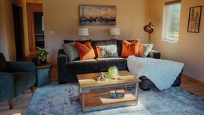 A cozy living room with a sofa, coffee table, and a painting on the wall. - In-Town Homer Hideaway 3BR/2BA (Homer)