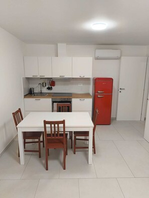 A compact kitchen with white cabinets, a red refrigerator, and a dining table with wooden chairs. - Villa d'aMare | Holiday apartments in Porto Potenza Picena - Corallo (Porto Potenza Picena)