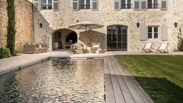 Un bâtiment en pierre doté d’une piscine, d’un espace extérieur aménagé et d’une terrasse en bois.