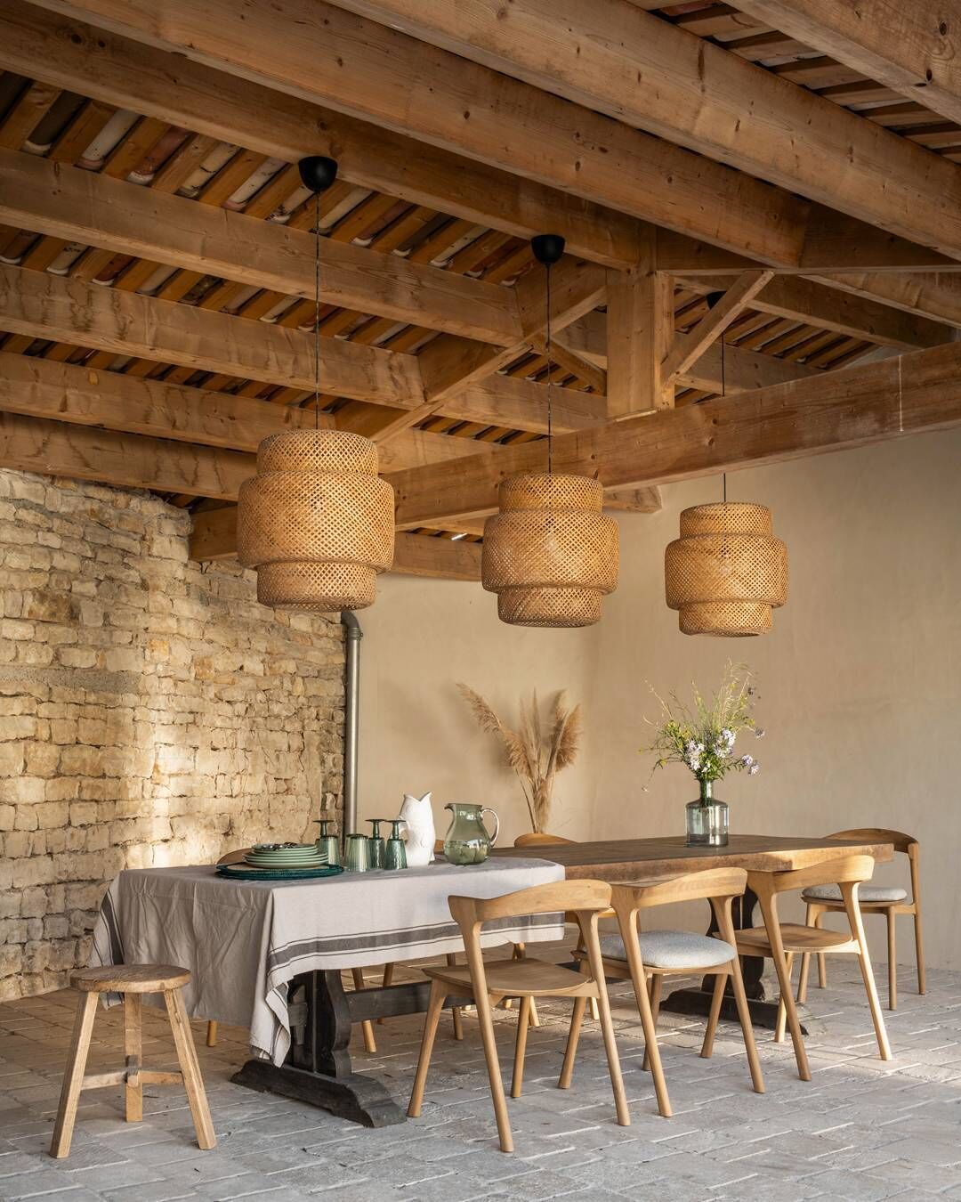 Ein rustikaler Essbereich mit einer Steinwand, Holzbalken und einem Tisch, der mit Stühlen und hängenden Korbtischen ausgestattet ist.