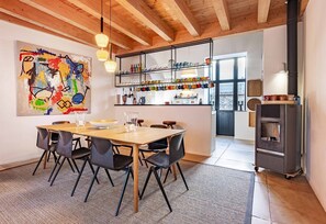 Una cocina moderna con techo de madera, una mesa de comedor con sillas, un cuadro abstracto de colores y una estantería empotrada con cristalería.