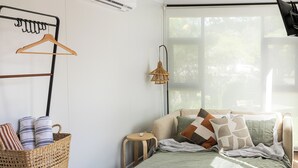 A bedroom with a bed, a hanging laundry rack, a wicker basket, and a window with natural light.