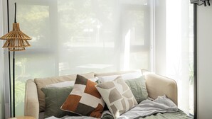 A bedroom with a large window, a bed with multiple pillows, a side table, and a wall-mounted TV.