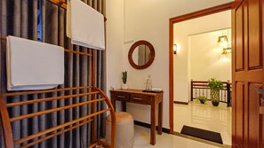 A hotel room with a wooden desk, a mirror, a towel rack, a small stool, and a potted plant. - Elegant Resort Hiriketiya (Dikwella)
