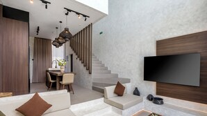 Un intérieur moderne avec un canapé, un panier de fruits, un escalier et un téléviseur à écran plat fixé au mur.