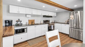 A modern kitchen with white cabinets, stainless steel appliances, and wooden beams on the ceiling.