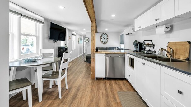A modern kitchen with white cabinets, a wooden ceiling beam, a built-in dishwasher, and a large window.