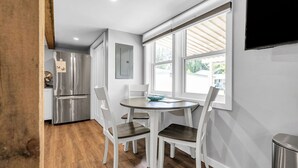 A modern kitchen with stainless steel appliances, a dining table with four chairs, and large windows providing natural light.