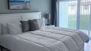 Un dormitorio con una cama grande, una mesita de noche, una lámpara, un cuadro y vistas por la ventana.