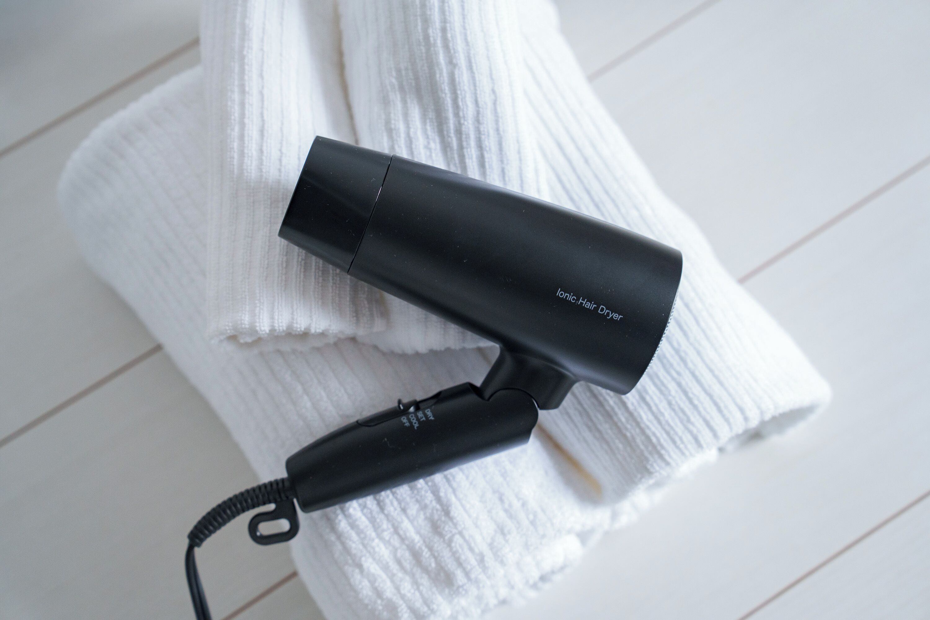 A black hair dryer with a cord, placed on a white towel.