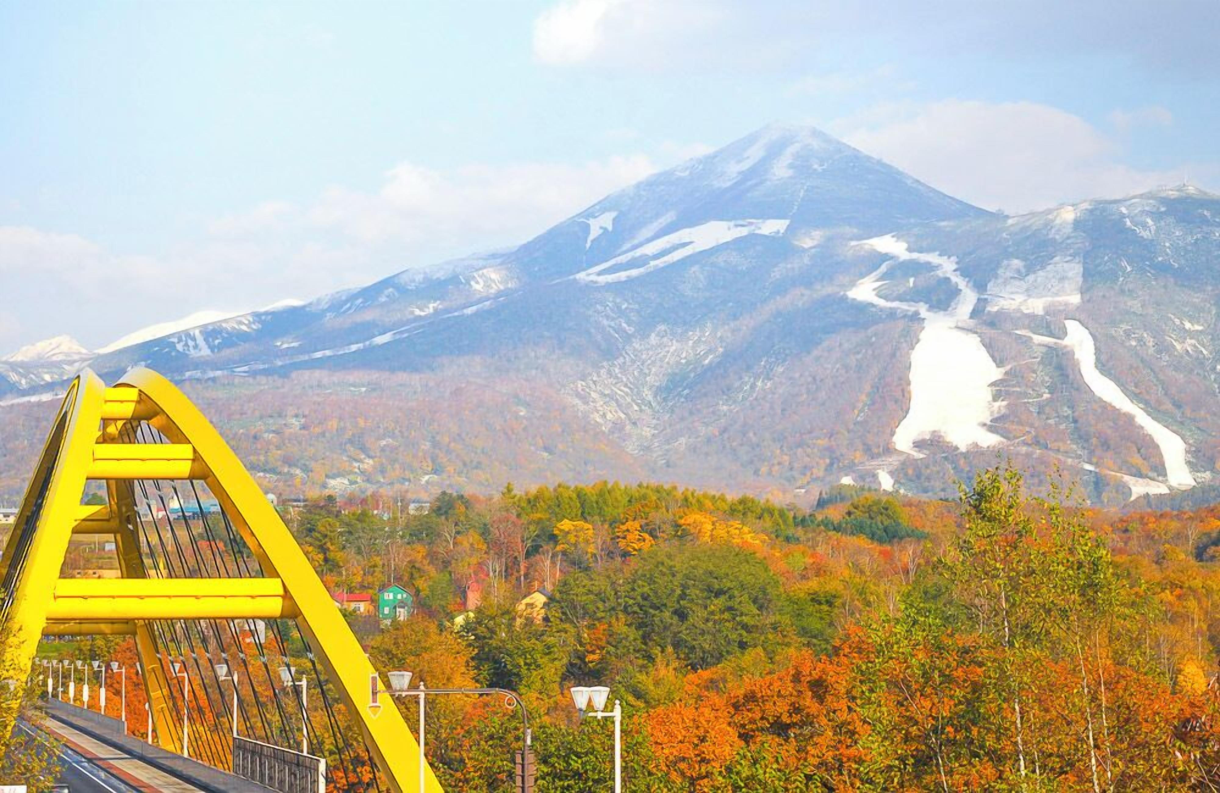 A yellow bridge with a view of a mountain and autumn foliage.