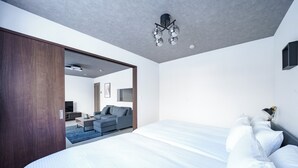 A modern hotel room with a large bed, a sofa, and a television in the adjacent living area. - HILLS NISEKO 105 (Niseko)