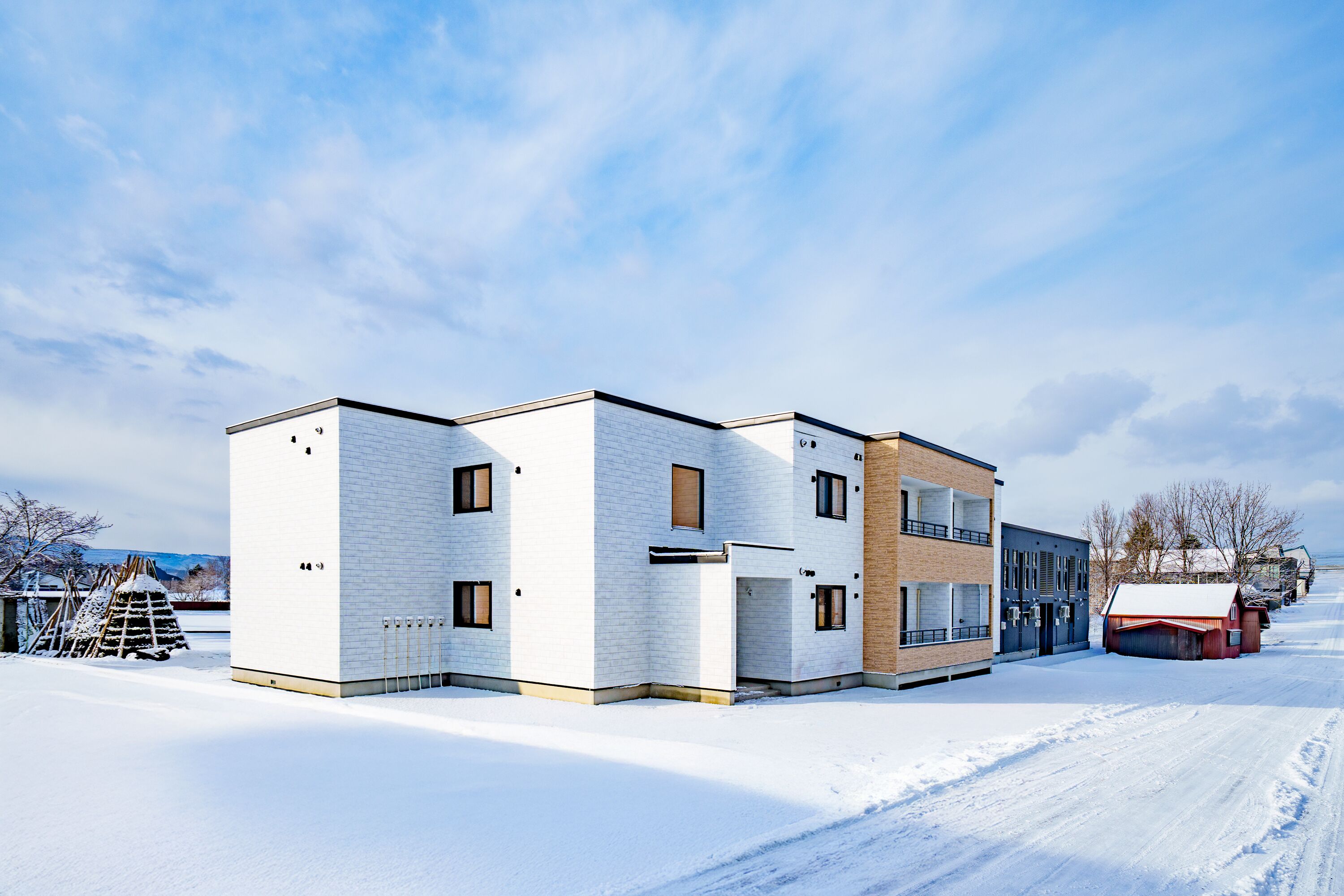 A modern multi-story building with a flat roof, large windows, and a snow-covered ground.