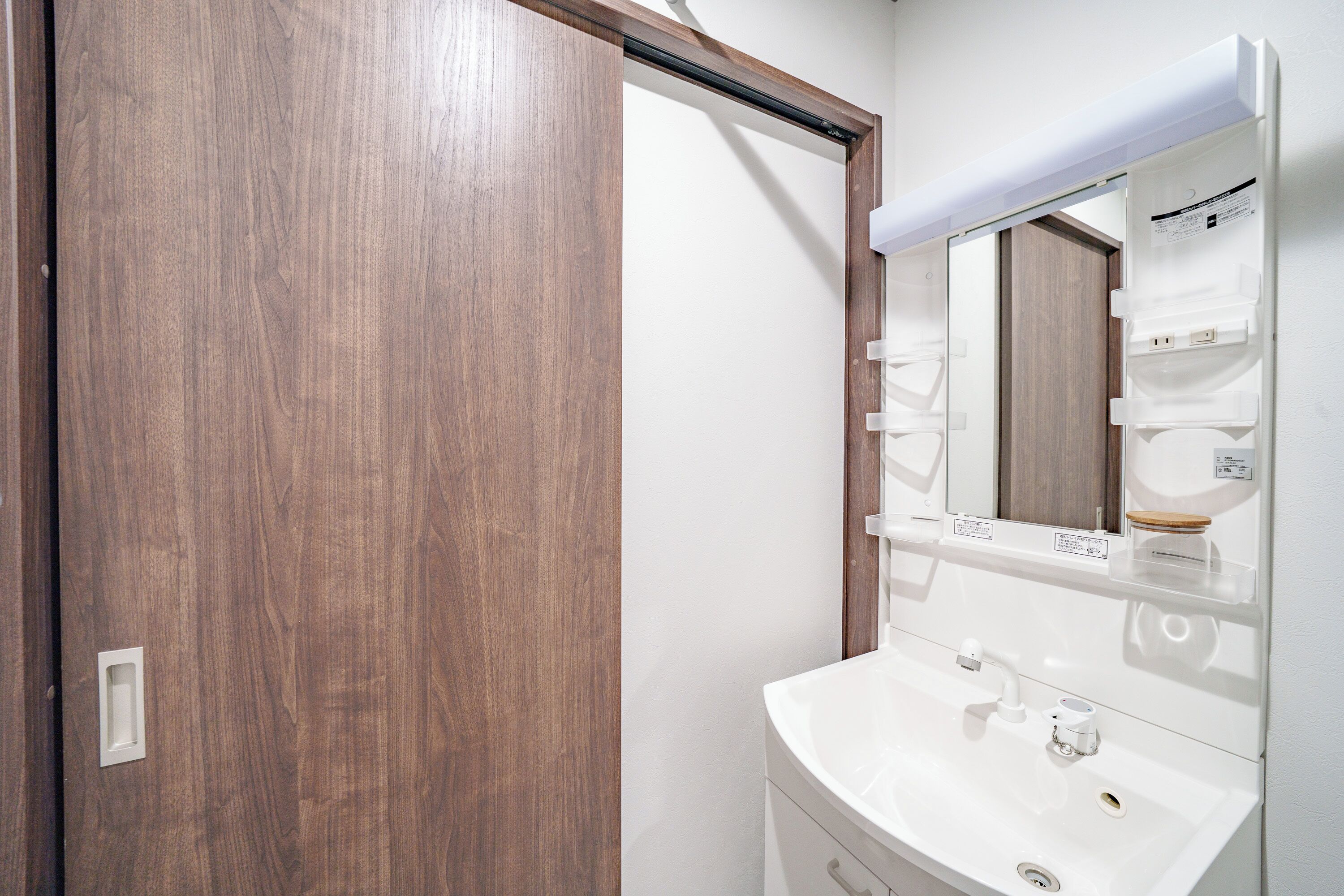 A bathroom with a wooden door, a white sink, and a mirror with a shelf above it.