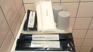 A bathroom with a white towel, two black toothbrush packets, and two gray bottles. - HotelSumi (Naha)
